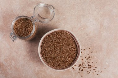 Pişmemiş organik karabuğday taneleri bir kasede ve açık bej arka planda cam kavanozda. Sağlıklı ve diyet gıda konsepti. Düz yatıyordu