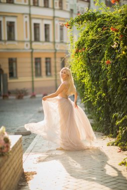 Güzel, gülümseyen, uzun sarı saçlı, zarif, hafif elbiseli genç bir kadın cadde boyunca koşuyor.