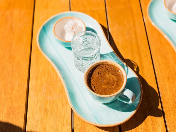 Cup of hot black turkish coffee in blue cup served with glass of water and sugar