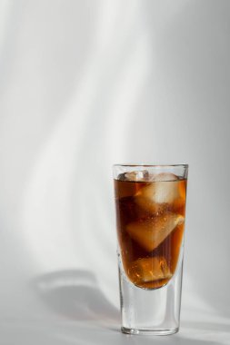 Beyaz zemin üzerinde buz olan bir bardak kola.