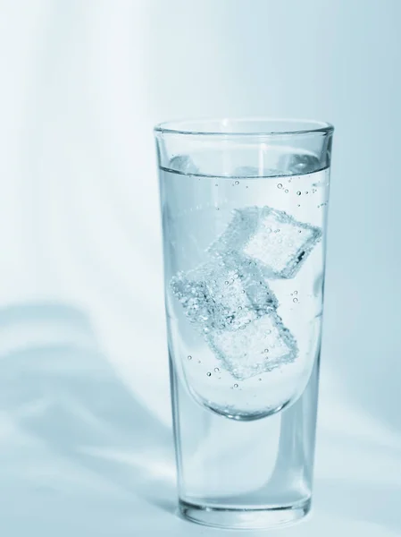 Glass of clean mineral sparkling water with ice on a light blue background