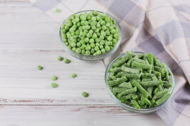 Beyaz ahşap arka planda farklı organik donmuş sebzelerle üst görünüm kompozisyonu. Bir kasede taze fasulye ve bezelye