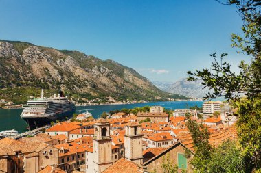 Eski kasabanın turuncu çatıları, tekneleri ve marina koyundaki büyük yolcu gemisi, deniz, dağlar, mavi gökyüzü olan renkli bir manzara. Karadağ 'ın Kotor Körfezi' nin üst manzarası