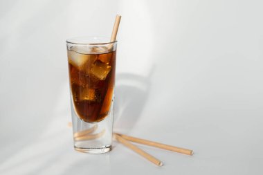 Beyaz arka planda buzlu ve samanlı bir bardak kola.