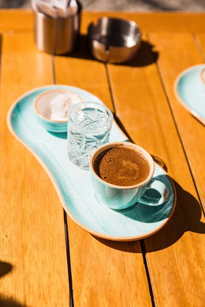 a cup of hot black turkish coffee in blue cup served with glass of water and sugar. street cafe