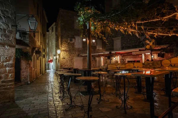 Karadağ 'ın eski Budva kentinde geceleri masa ve sandalyeli boş sokak kafesi terası.