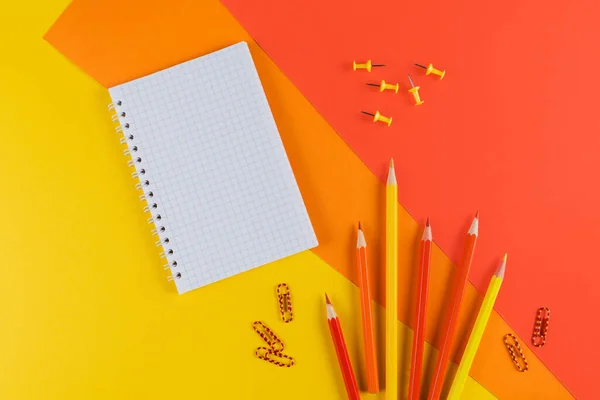 Yellow and orange office desk table with blank notebook and other office supplies. Top view with copy space, flat lay.
