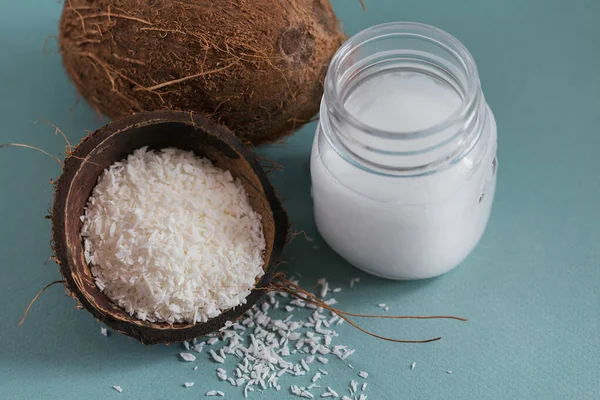 Coconut, coco flakes and coconut oil in jar on light blue background. Healthy cooking concept