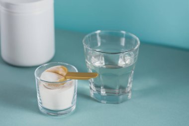 Kolajen içeren cam suda çözünmüş ve açık mavi masada kolajen protein tozu var. Sağlıklı yaşam tarzı kavramı.