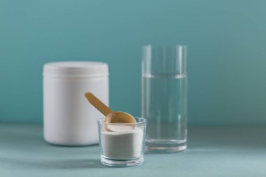 Kolajen içeren cam suda çözünmüş ve açık mavi masada kolajen protein tozu var. Sağlıklı yaşam tarzı kavramı.