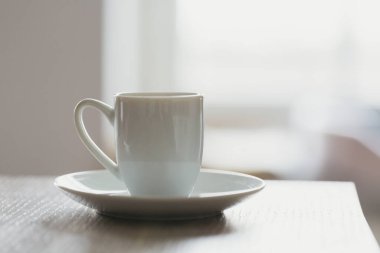 Pencerenin karşısındaki masada beyaz bir fincan sabah kahvesi.