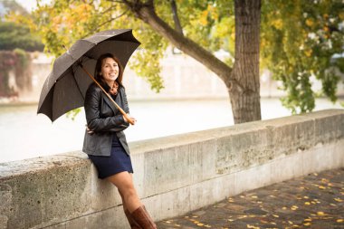 Siyah ceketli esmer kadın nehir kenarında duruyor.