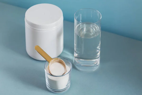 Glass with collagen dissolved in water and collagen protein powder on light blue table — Stock Photo, Image