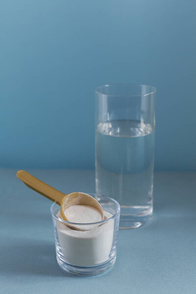Collagen powder in bowl, glass of water and measure spoon on light blue background