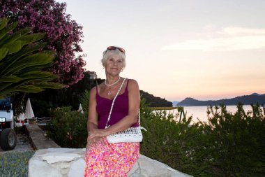 Sunset 'te deniz kenarında dinlenen kıdemli kadın.