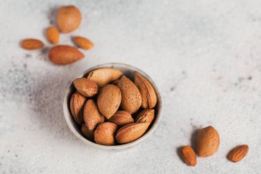 Beyaz arka planda bir kâse dolusu badem fıstığı. Kabuklarında taze fındık.