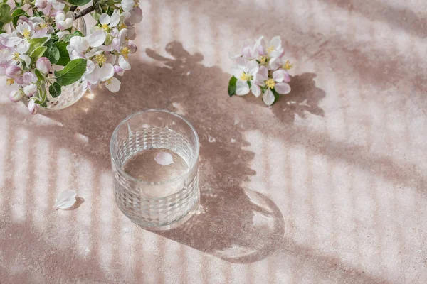 Un vaso de agua sobre la mesa con una rama de manzano en flor en un vaso — Foto de Stock