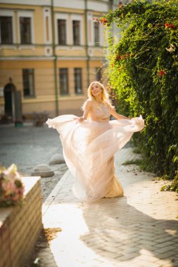 Güzel, gülümseyen, uzun sarı saçlı, zarif, hafif elbiseli genç bir kadın cadde boyunca koşuyor.