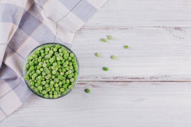 Beyaz ahşap arka planda organik donmuş sebzelerle üst görünüm. Kavanozda yeşil bezelye.