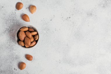 Beyaz arka planda bir kâse dolusu badem fıstığı. Kabuklarında taze fındık. Metin için boş alanı olan üst görünüm