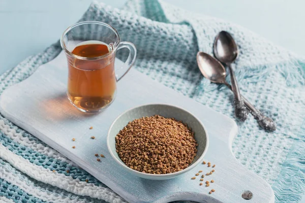 Bir bardak Mısır çemen çayı, Helba ya da Methi Dana içkisi ve açık mavi arka planda çemen otu tohumu
