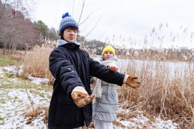 Ergen çocuk kollarını uzatıyor. Annesi ona doğru uzanıyor. Doğadaki aydınlık kış aktiviteleri sırasında.