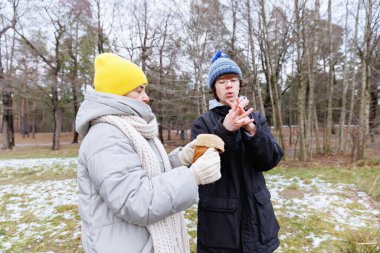 Genç çocuk soğuk ormanda yürürken annesinin yanında durup eldiven verirken donmuş parmaklarını tutuyor.