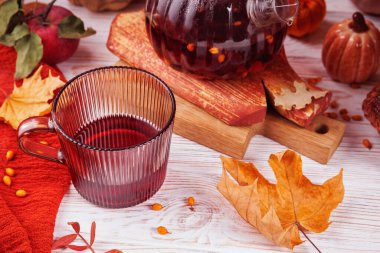 Çay fincanındaki kırmızı bitki çayı çaydanlıklı, deniz dikenli, balkabaklı, akçaağaç yapraklı ve beyaz ahşap elmalı.