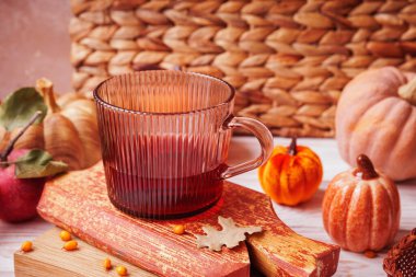 Kabaklar, elmalar, deniz dikenleri ve dokuma arkaplanlı kabaklar üzerine yerleştirilmiş sıcak bitkisel çaylı kaburgalı cam bardak.