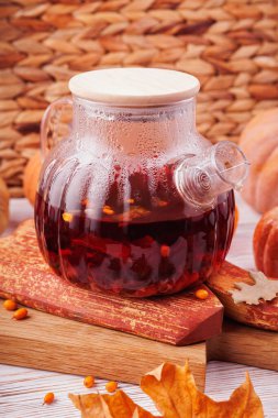 Kırmızı bitki çayı ve buharlı cam çaydanlık, sonbahar yaprakları ve balkabaklarıyla kırsal ahşap üzerine konur.