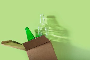 Geri dönüşümlü yeşil ve şeffaf şişeleri olan karton bir kap. Güçlü ışık tarafından aydınlatılıyor. Sanatsal gölgeler bırakıyor.