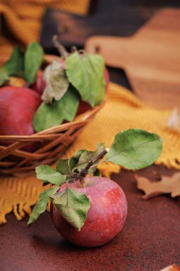 Yeşil yapraklı taze kırmızı elma. Sonbahar elementli sarı desenli kumaş üzerinde elma sepeti.