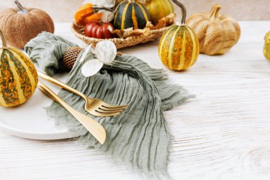 Yeşil peçete, altın çatal bıçak, dekoratif balkabağı, hasır sepet ve ahşap yüzeyde yumuşak kumaş detaylarıyla kırsal sonbahar masası kurulumu.