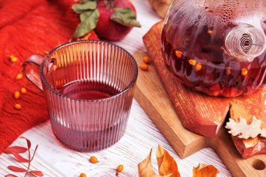 Deniz dikenleri, yapraklar ve elmalarla çevrili kırmızı bitki çayı ve rustik tahtaların üzerinde çaydanlık.