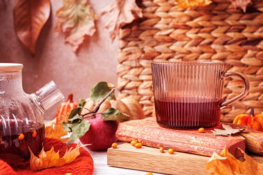 Kırsal kırmızı panolarda kırmızı bitkisel çaylı kaburgalı cam bardak elma, kuru yapraklar ve sonbahar ayrıntılarıyla çevrili.