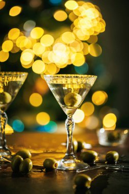Tek yeşil zeytinli bir martini bardağı, altın renkli ışıkların arkaplanına nazikçe yerleştirilmiş, güzel bir yemek ve kutlamanın özünü yakalıyor..