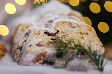 Dilimlenmiş noel aromalı, toz şekerle kaplanmış, badem, kozalak ve bulanık altın renkli ışıklarla çevrili, sıcak bir tatil atmosferini çağrıştıran bir ekmek..