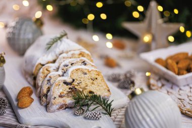 Geleneksel Noel süslerinin yakın çekimi toz şekerle kaplanmış, bademler, çam dalları ve arka planda bulanık ışık ve ahşap kesme tahtasındaki Noel süsleriyle çevrili.