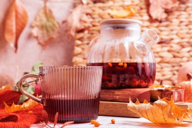 Sonbahar yaprakları ve kırsal elementlerle çevrili kırmızı eritilmiş çaydanlığın yanında sıcak bitkisel çay ile cam bardak.