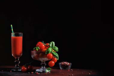 Taze vişneli domateslerin yanında domates suyu, yeşil fesleğenli cam kase ve arka planda biber karışımı.