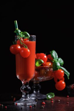 Uzun bardakta domates kokteyli, kiraz domatesli fesleğen ve karamsar ışıkta koyu arka planda garnitür.