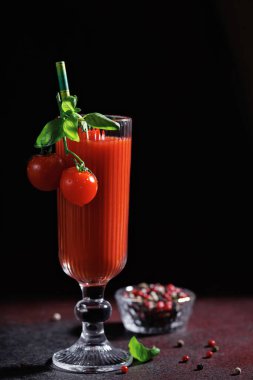 Uzun bardakta domates kokteyli, fesleğen ve kiraz domatesli, koyu kırsal bir masada, biber karışımının yanında.