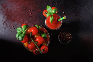 Üzerinde fesleğenli domates suyu, yanında bir kase kiraz domatesi ve kırsal masa yüzeyine saçılmış biberler.