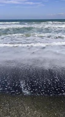 Okyanus dalgalarının geniş görünümü karanlık kumlu sahile yuvarlanırken görülebilir ufuk doğal ışık ve sakin atmosfer altında yüksek kaliteli 4K görüntü