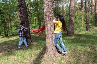 Annesi nihai düğümünü atarken, oğlu orman pikniğinde hamak tutmaya yardım ediyor.
