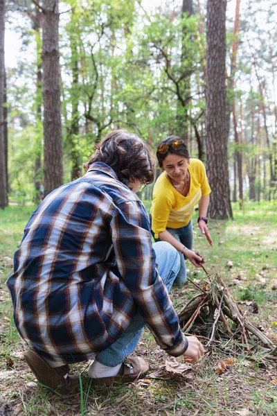 Genç çocuk ve annesi bahar pikniği sırasında yeşil bir ormanda dal kullanarak ateş yakmak için birlikte çalışıyorlar.