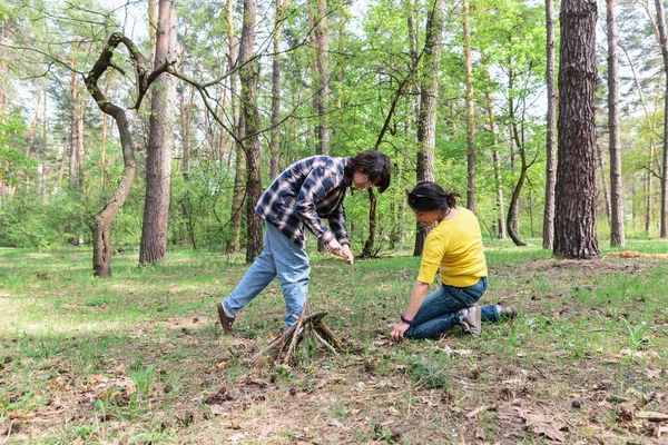Genç bir çocuk ve annesi ormanda yangın çıkarıyorlar. Aile kampı ve hayatta kalma becerileri pratiği sırasında sopalarla ateş yakıyorlar.
