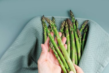 Sağlıklı yemek hazırlamak için havludan çiğ yeşil kuşkonmaz mızrakları tutan kadın ellerini kapat.