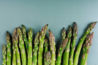 Kuşkonmaz başlıklarının makro üst görünümü temiz pastel mavi arka plan üzerinde su damlacıkları ile mutfak ve sağlık temaları için