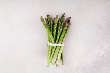 Taze yeşil kuşkonmaz mızraklarının üst görüntüsü beyaz iplikle bağlanmış hafif taştan bir arka planda